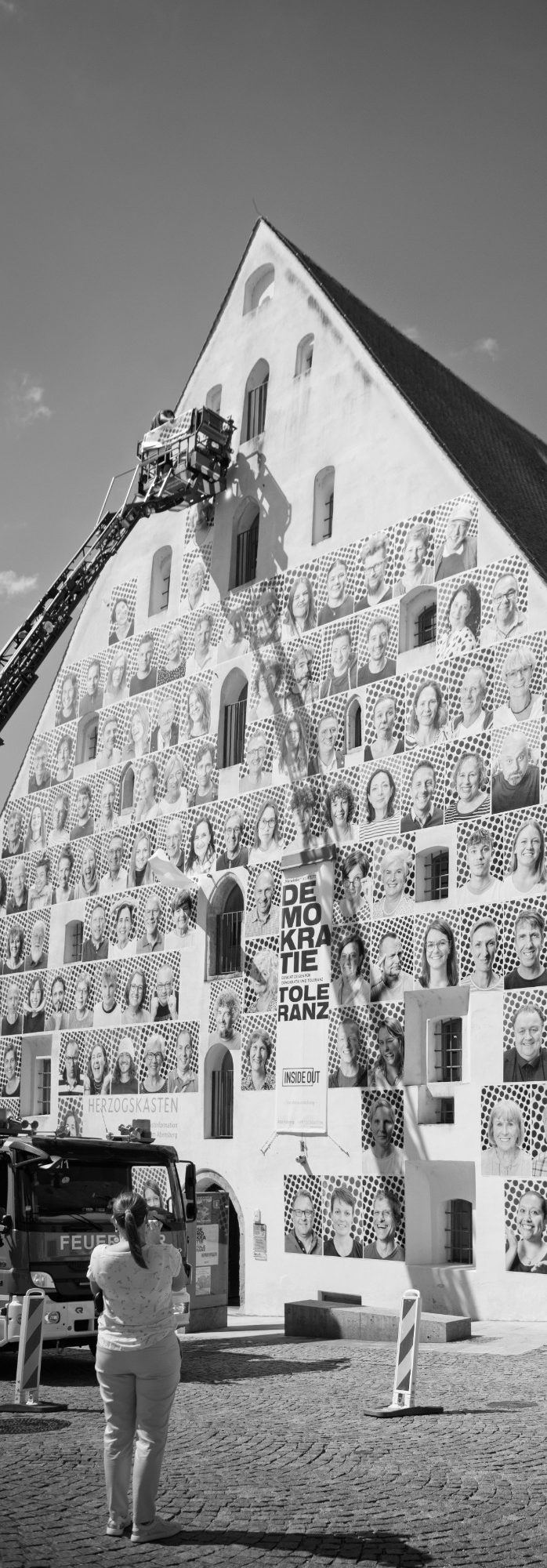 Installation InsideOut Fassade des Herzogskastens mit InsideOut-Porträts, Personen auf Drehleiter und zuschauende Menschen.