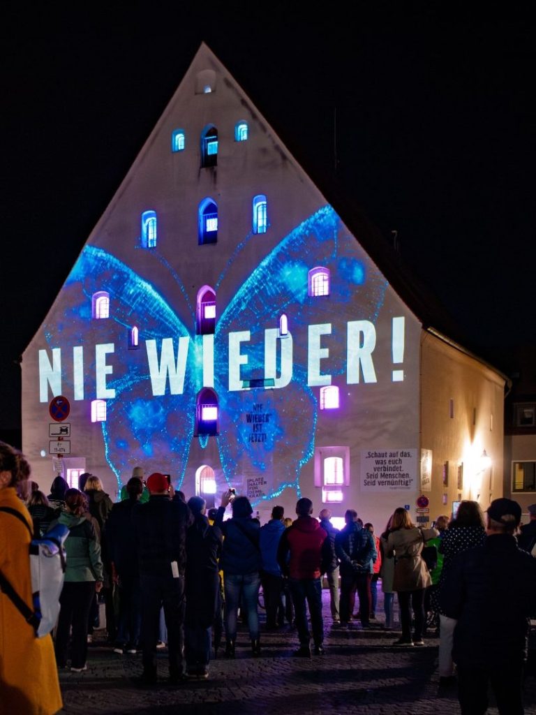 Laser/Lichtshow Menschenmenge vor dem Herzogskasten mit Laserprojektion ‚NIE WIEDER!‘ auf der Fassade bei Nacht.