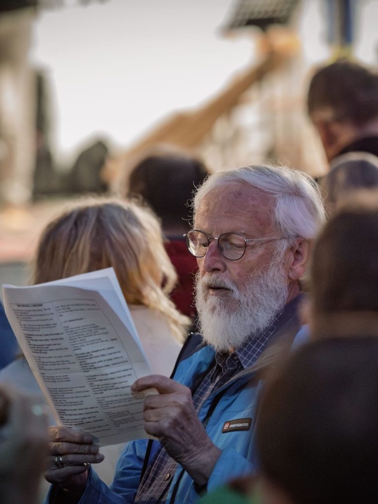 Popup Chor Mehrere Personen im Freien, eine hält ein Blatt mit Liedtexten und singt im PopUp-Chor.